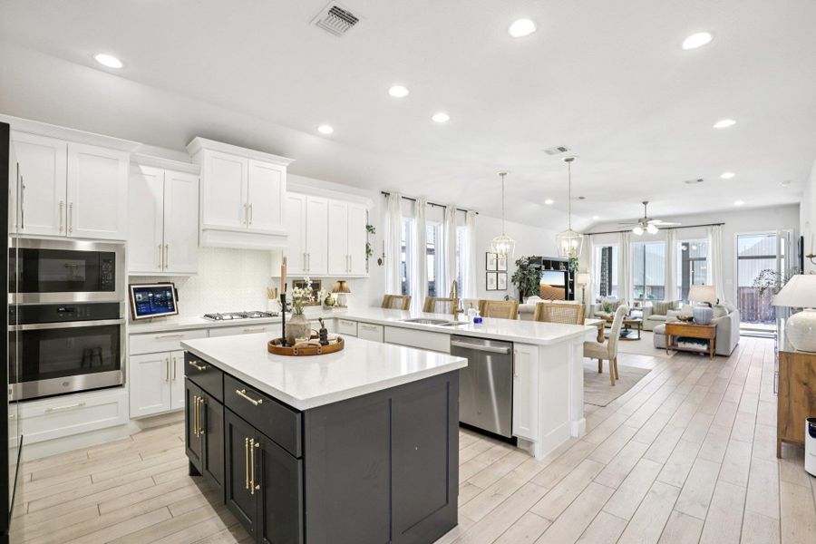 Two tone kitchen featuring open floor plan, decorative light fixtures, a peninsula, a center island, and stainless steel appliances