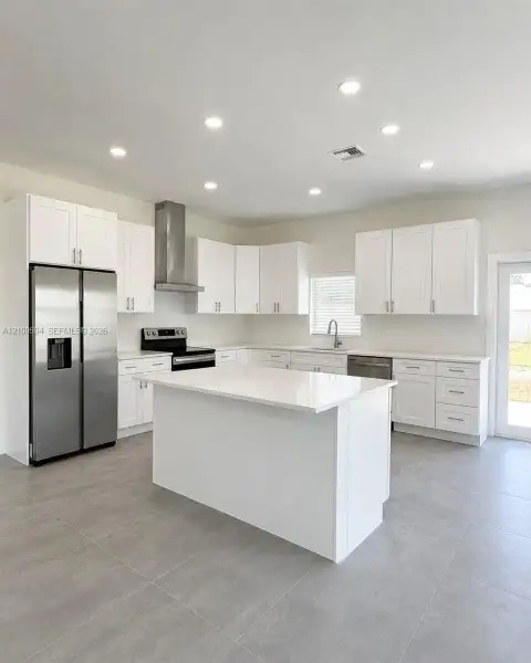 Kitchen featuring white cabinetry, a center island with a quartz countertop, stainless steel appliances, a stainless steel range hood, and large-format tile flooring