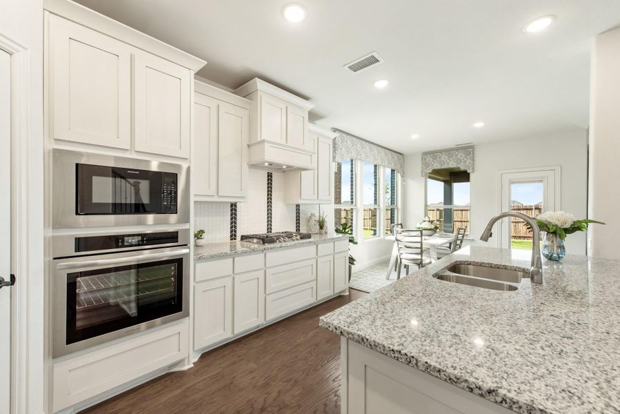 Kitchen with white cabinets, granite island, stainless steel appliances, and hardwood floors open to dining area