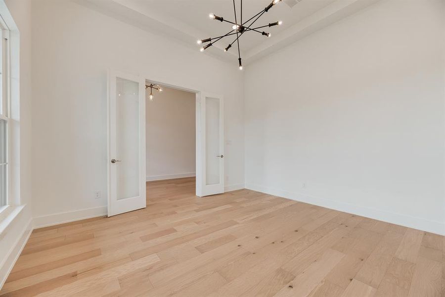 Spare room with a chandelier, light wood finished floors, and french doors