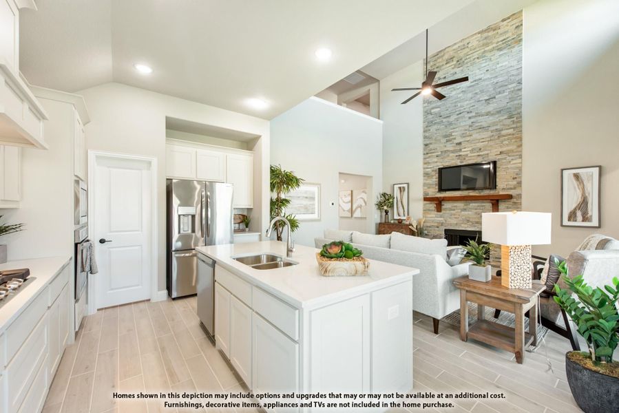 Open-concept kitchen with white island and cabinets flowing into living room with stone fireplace and vaulted ceiling Open-concept kitchen with white island and cabinets flowing into living room with stone fireplace and vaulted ceiling