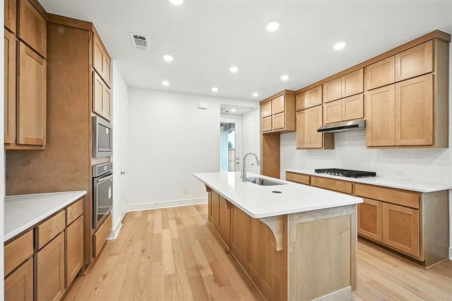 Kitchen with light stone counters, light wood-style flooring, recessed lighting, tasteful backsplash, and stainless steel appliances Kitchen with light stone counters, light wood-style flooring, recessed lighting, tasteful backsplash, and stainless steel appliances