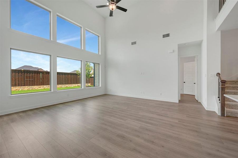 Vaulted living area featuring a ceiling fan, abundant natural light from multi-level windows, wood-finish flooring, and a staircase with a carpeted runner and dark wood handrail Vaulted living area featuring a ceiling fan, abundant natural light from multi-level windows, wood-finish flooring, and a staircase with a carpeted runner and dark wood handrail