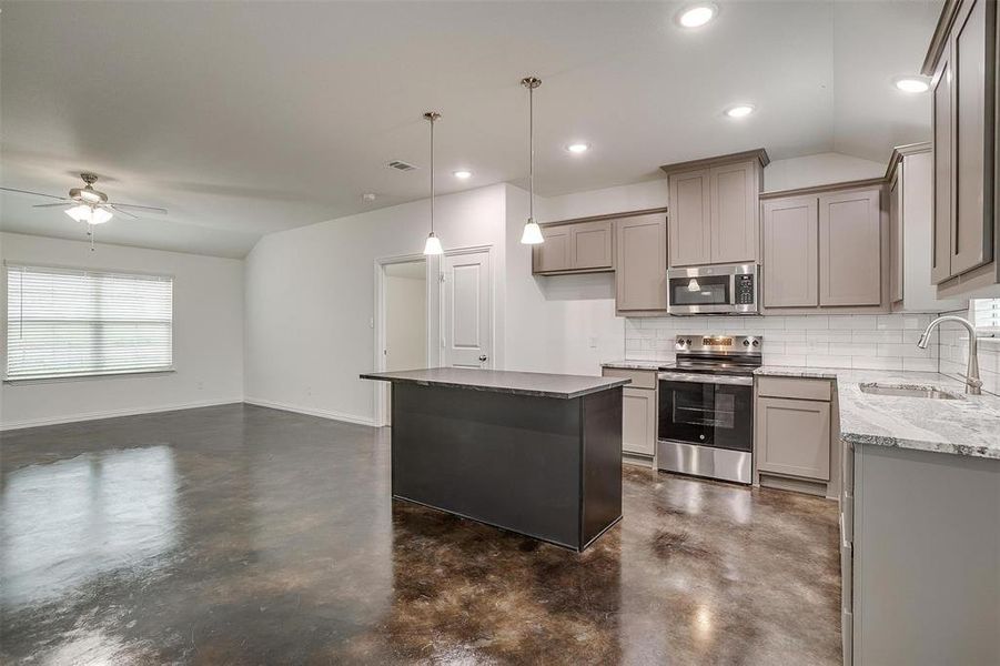 Kitchen with stainless steel appliances, decorative backsplash, lofted ceiling, gray cabinetry, and a center island
