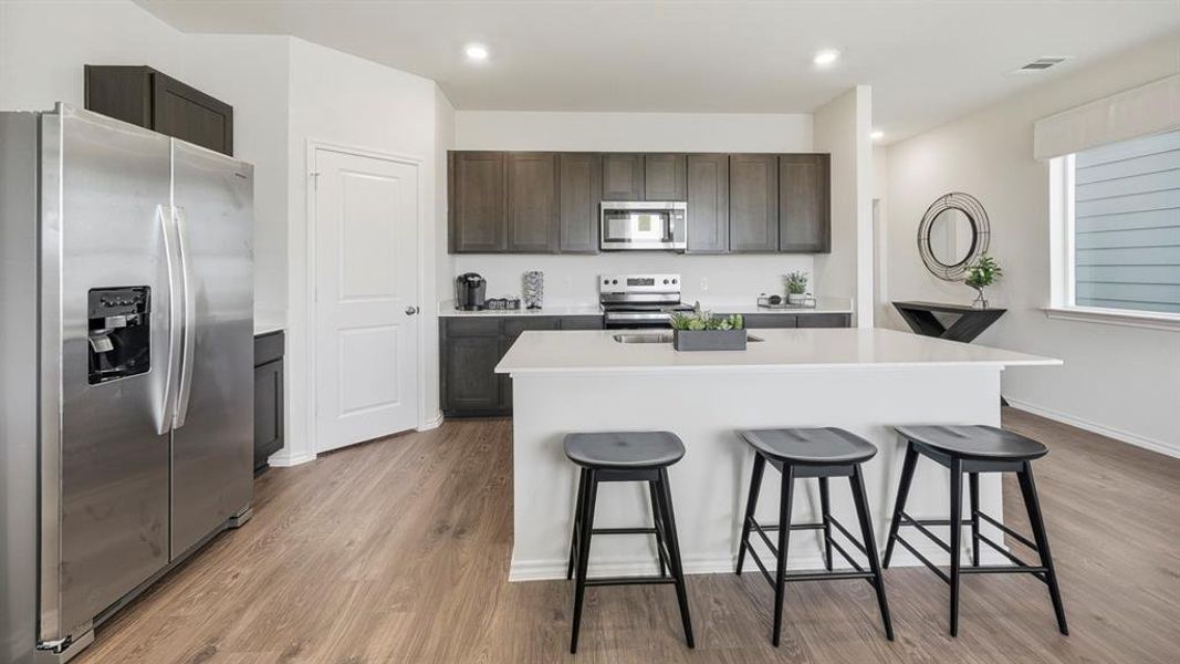 Kitchen with stainless steel appliances, dark wood finished floors, a kitchen island with sink, a breakfast bar area, and dark brown cabinetry Kitchen with stainless steel appliances, dark wood finished floors, a kitchen island with sink, a breakfast bar area, and dark brown cabinetry