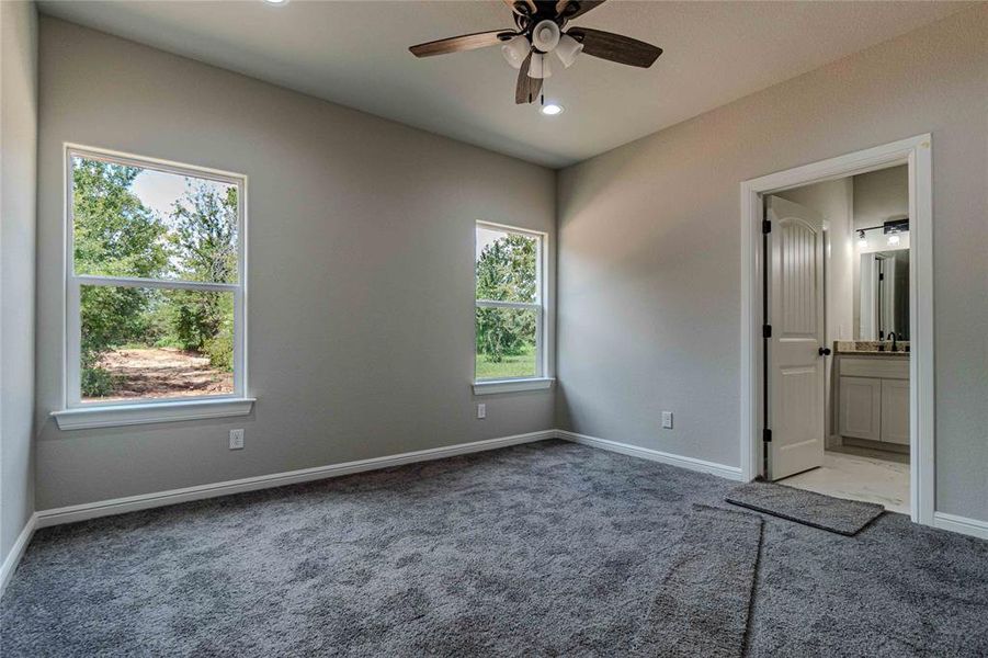 Unfurnished bedroom with ensuite bath, multiple windows, ceiling fan, and light colored carpet