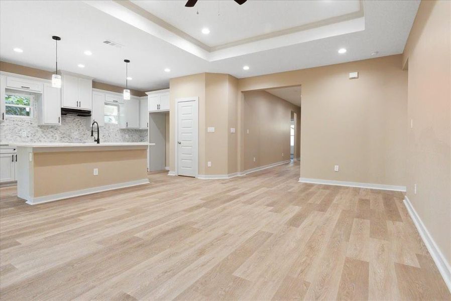 Kitchen featuring white cabinets, an island with sink, backsplash, light hardwood / wood-style flooring, and decorative light fixtures