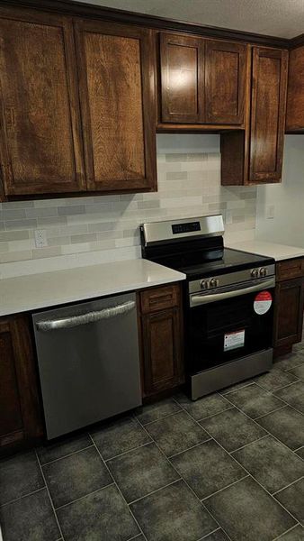 Kitchen featuring stainless steel stove, dark brown cabinetry, dishwashing machine, and decorative backsplash