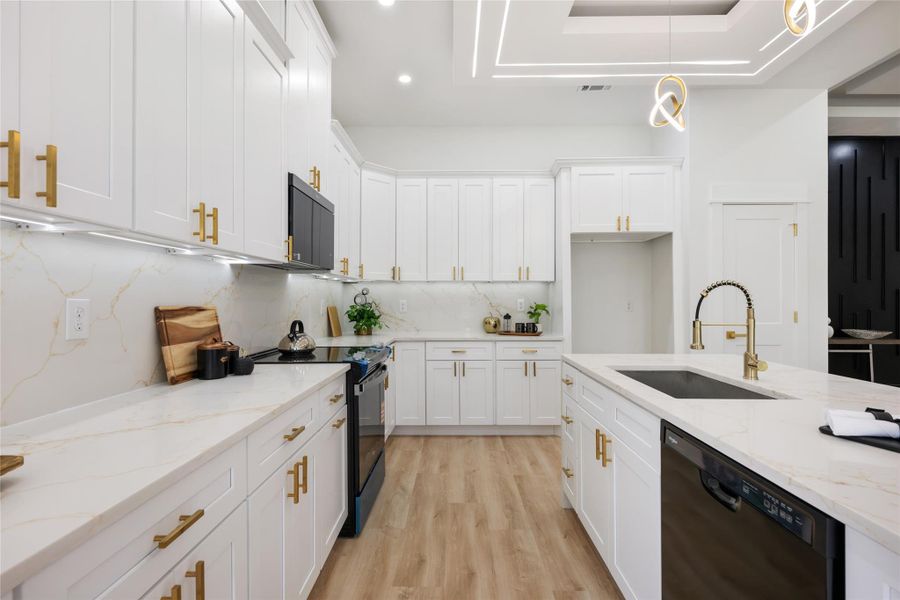 Modern kitchen featuring white cabinetry with gold-tone hardware, a large central island with an undermount sink, light wood-finish flooring, and white countertops with a subtle veining pattern