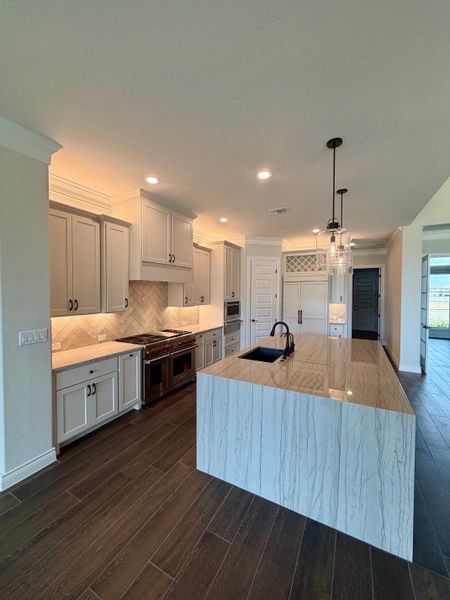 Rich wood-look tile flooring and a waterfall-edge stone island anchor this modern kitchen.