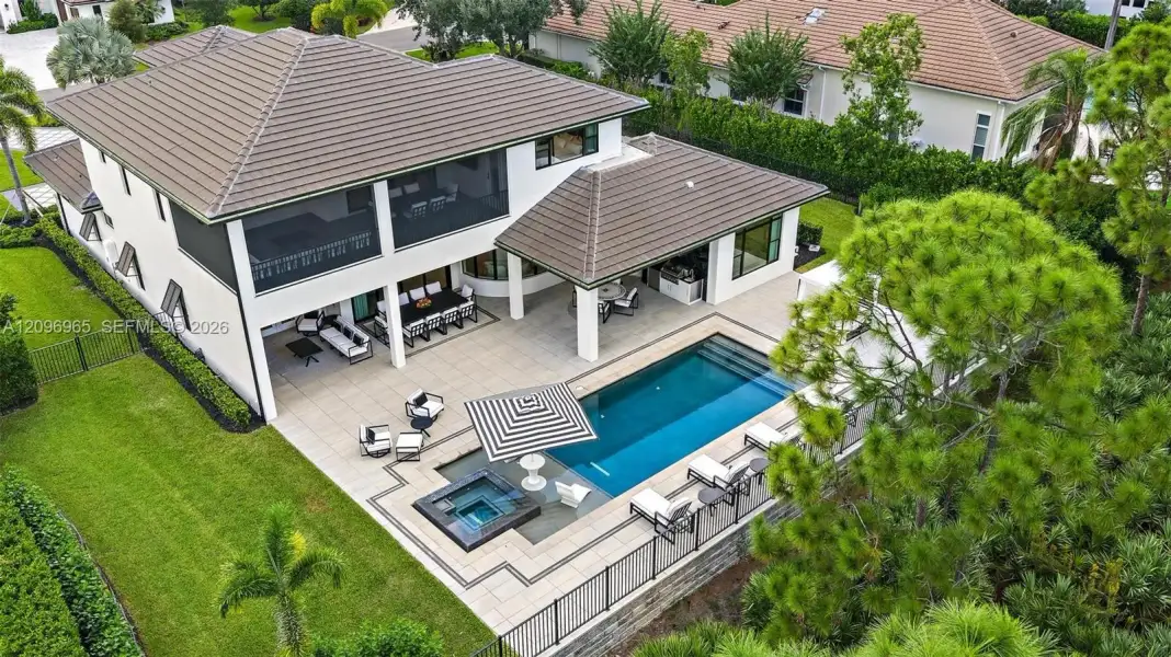 Two-story residence featuring a tile roof, an expansive stone-paved patio, a built-in swimming pool with an integrated spa, and a covered lanai