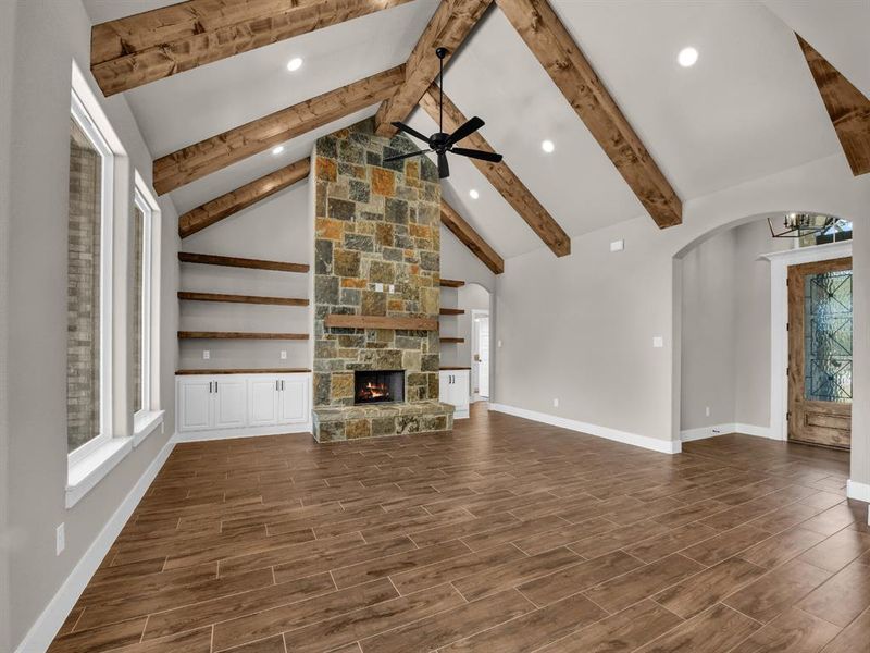 Unfurnished living room with plenty of natural light, wood tiled floors, high vaulted ceiling, beamed ceiling, and a stone fireplace