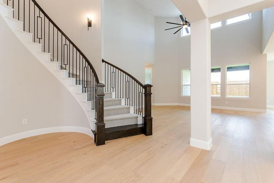 Staircase featuring ceiling fan, light wood-type flooring, and a towering ceiling