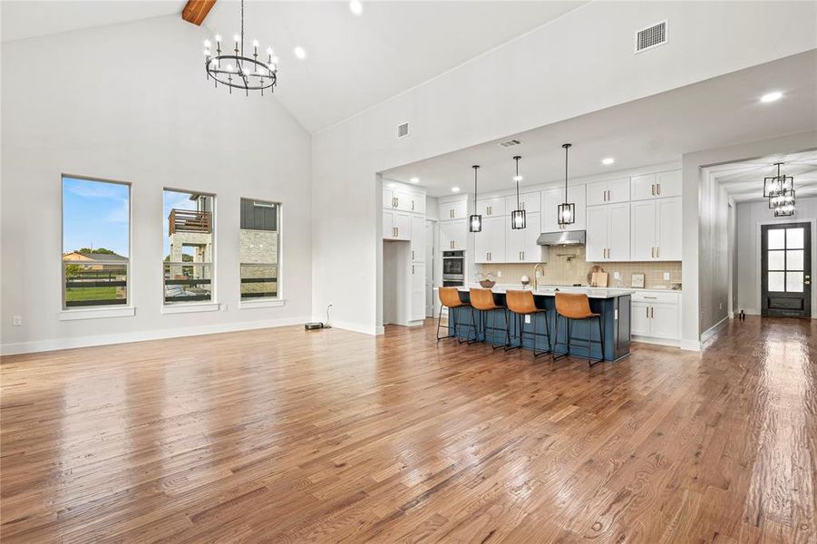 Unfurnished living room featuring a chandelier, light wood-type flooring, high vaulted ceiling, recessed lighting, and beam ceiling Unfurnished living room featuring a chandelier, light wood-type flooring, high vaulted ceiling, recessed lighting, and beam ceiling