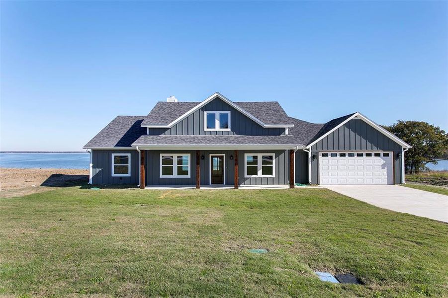 View of front of property with a front lawn, a water view, covered porch, and a garage