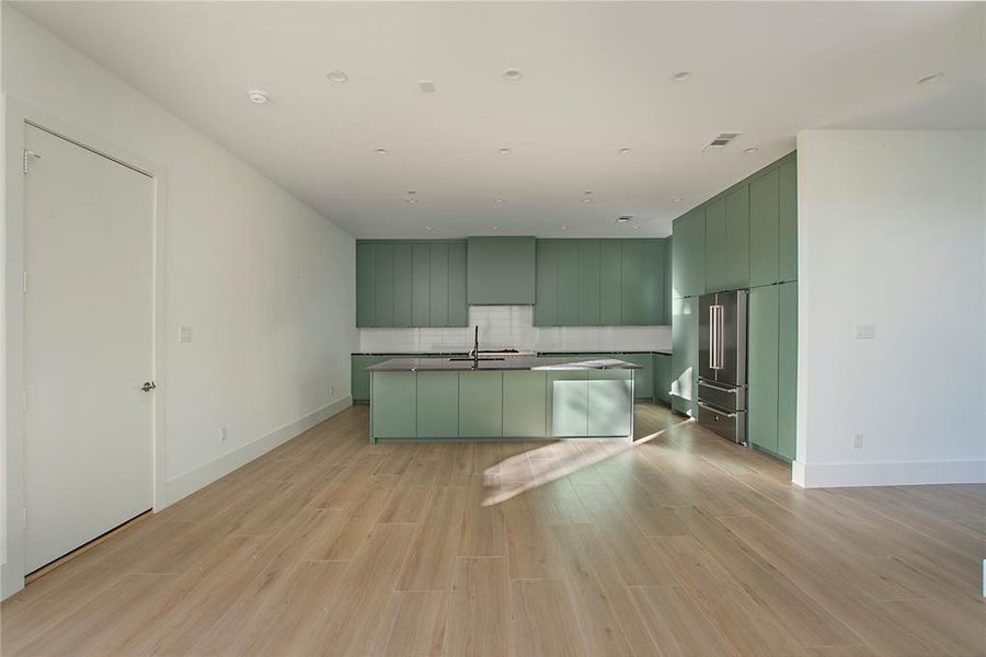 Kitchen with an island with sink, light hardwood / wood-style flooring, green cabinets, and high end fridge