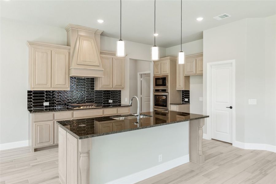 Kitchen with cream cabinets, dark granite island, black tile backsplash, and pendant lights over sink Kitchen with cream cabinets, dark granite island, black tile backsplash, and pendant lights over sink