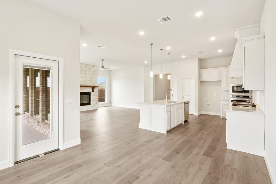 Open-concept kitchen and living area with white cabinets, center island, hardwood floors, and stone fireplace.