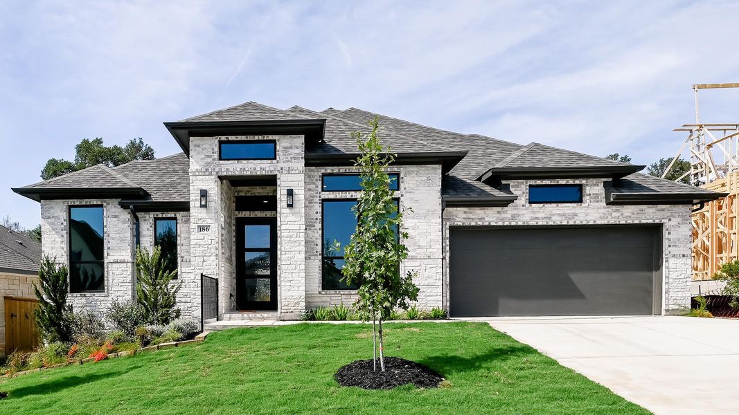 View of front of home with a shingled roof, stone siding, concrete driveway, and an attached garage