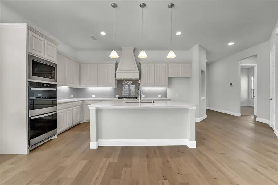 Kitchen featuring pendant lighting, stainless steel appliances, a kitchen island with sink, light wood finished floors, and tasteful backsplash