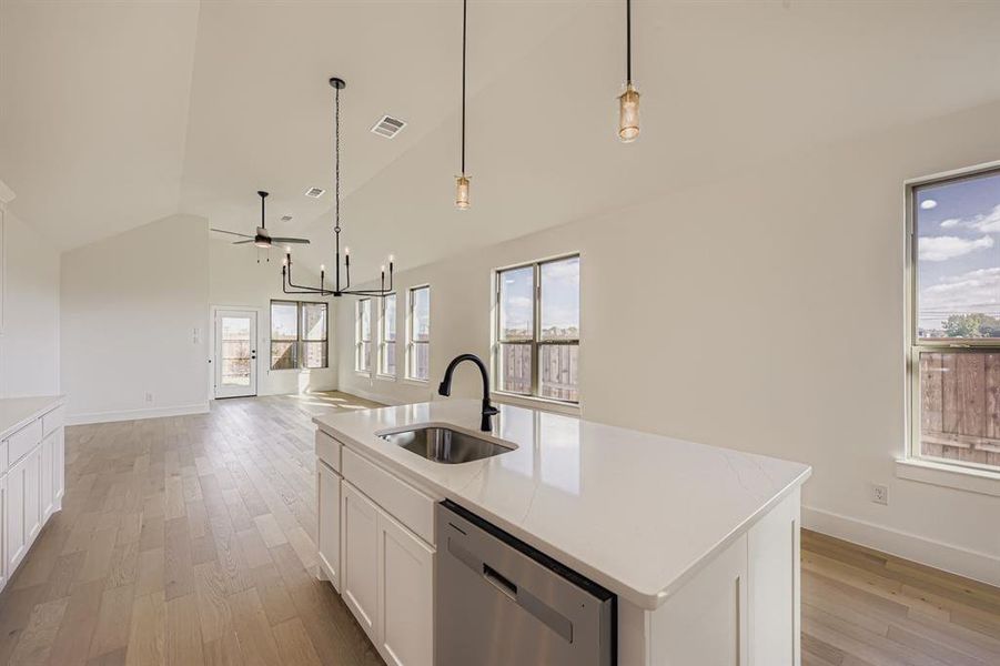 Kitchen featuring white cabinetry, pendant lighting, an island with sink, light wood finished floors, and stainless steel dishwasher Kitchen featuring white cabinetry, pendant lighting, an island with sink, light wood finished floors, and stainless steel dishwasher