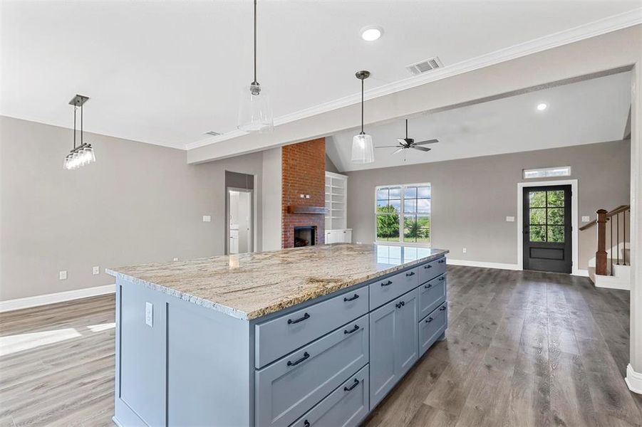 Kitchen with a center island, hardwood / wood-style flooring, a brick fireplace, hanging light fixtures, and vaulted ceiling