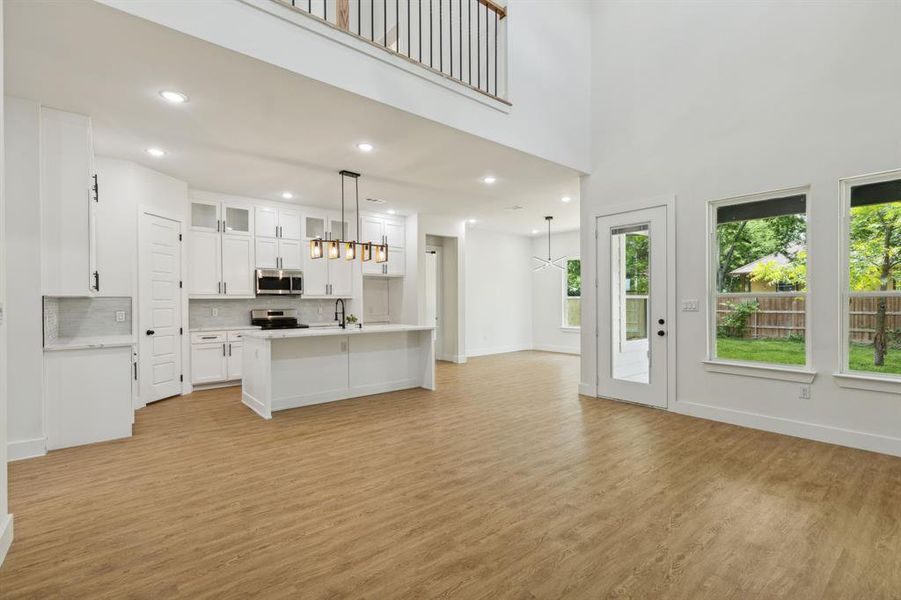 Kitchen featuring hanging light fixtures, appliances with stainless steel finishes, an island with sink, and light hardwood / wood-style flooring