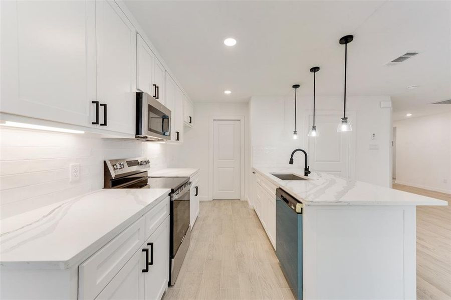 Kitchen with pendant lighting, white cabinetry, an island with sink, sink, and stainless steel appliances