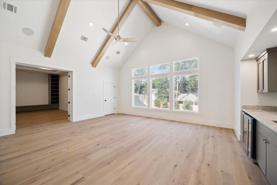 This spacious room features high vaulted ceilings with exposed wooden beams, large windows offering plenty of natural light, and warm wood flooring. There's a modern ceiling fan and adjacent to the theater room with built-in shelving. A sleek kitchenette with a mini-fridge is also present, making it ideal for entertaining. This spacious room features high vaulted ceilings with exposed wooden beams, large windows offering plenty of natural light, and warm wood flooring. There's a modern ceiling fan and adjacent to the theater room with built-in shelving. A sleek kitchenette with a mini-fridge is also present, making it ideal for entertaining.
