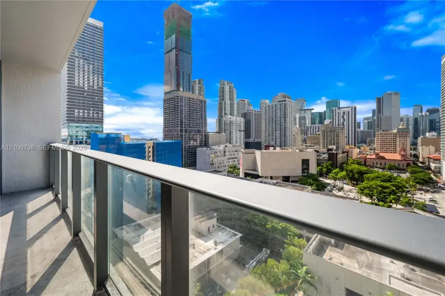 Private balcony featuring a glass panel railing with a metal handrail and expansive urban skyline scenery Private balcony featuring a glass panel railing with a metal handrail and expansive urban skyline scenery