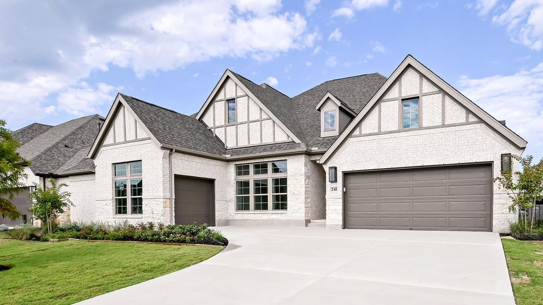 Tudor house with roof with shingles, brick siding, driveway, and stone siding