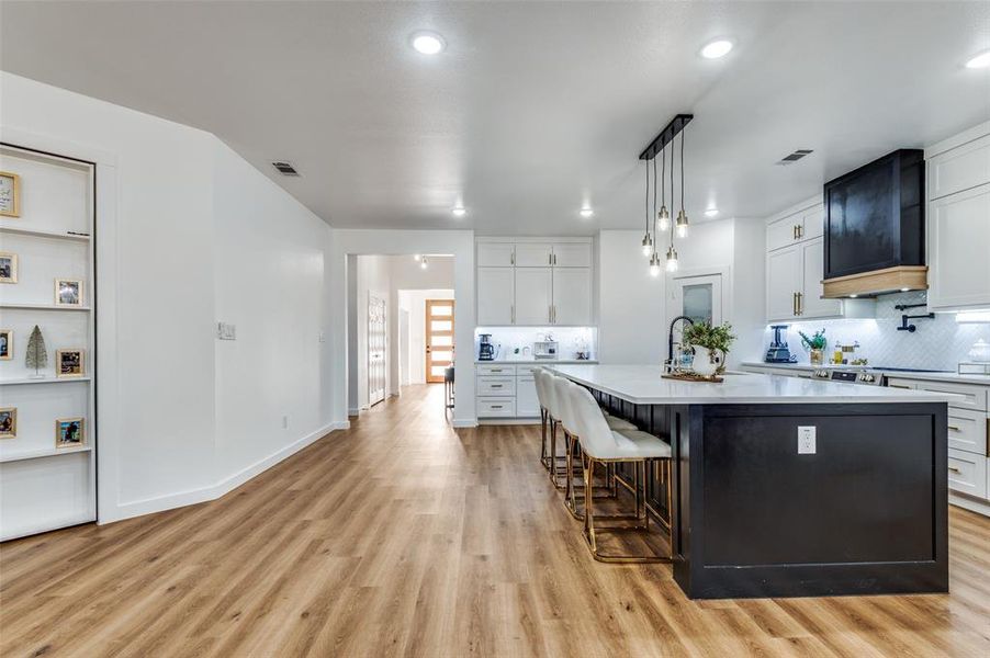 Kitchen with white cabinets, a breakfast bar, a center island with sink, hanging light fixtures, and backsplash