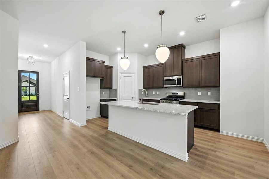 Kitchen featuring appliances with stainless steel finishes, dark brown cabinets, light wood finished floors, tasteful backsplash, and recessed lighting