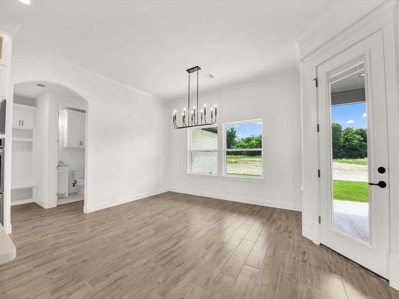 Unfurnished dining area with light wood-type flooring, crown molding, baseboards, and a chandelier