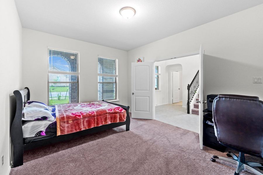 Carpeted room featuring two arched windows with blinds, a recessed ceiling light, and an open doorway leading to a staircase with dark banisters
