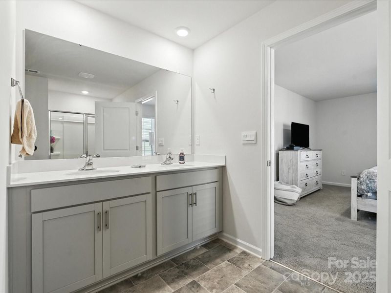 Elegant dual vanity with white countertops, gray shaker-style cabinetry, and large mirror. Ample storage and counter space make this primary bathroom both beautiful and highly functional.