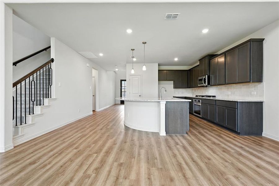 Kitchen featuring recessed lighting, decorative backsplash, light wood-type flooring, decorative light fixtures, and a kitchen island with sink