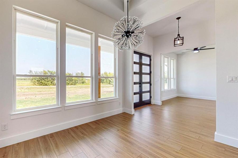 Spare room featuring light hardwood / wood-style floors, beamed ceiling, ceiling fan with notable chandelier, and plenty of natural light