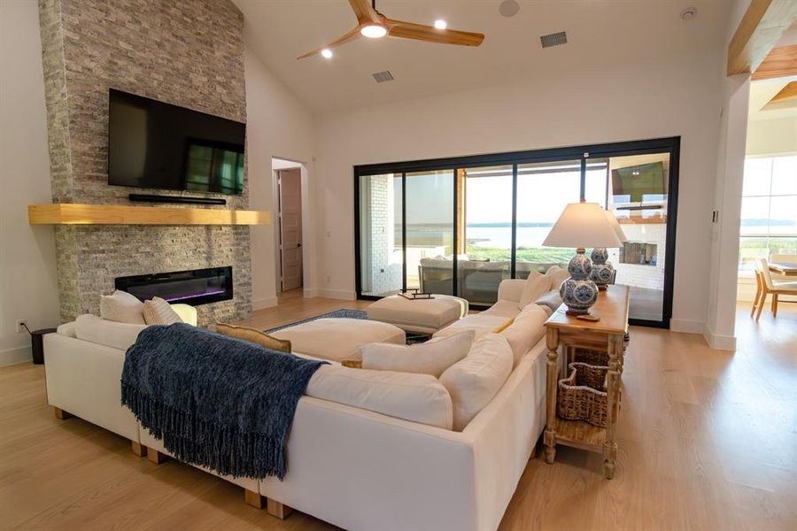 Living area featuring high vaulted ceiling, a fireplace, light wood-style floors, a ceiling fan, and recessed lighting Living area featuring high vaulted ceiling, a fireplace, light wood-style floors, a ceiling fan, and recessed lighting