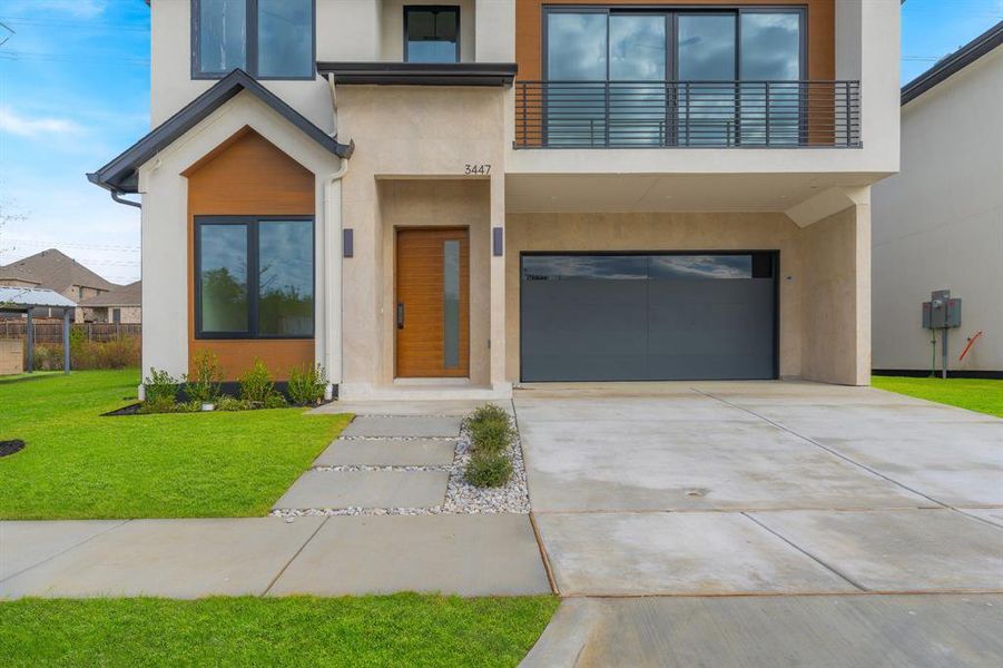 Contemporary house featuring stucco siding, a front yard, concrete driveway, an attached garage, and a balcony
