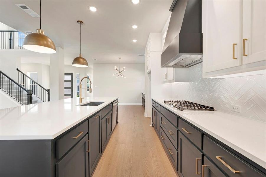 Two tone kitchen featuring light wood-style flooring, two tone cabinets, suspended lighting, a spacious island, and light stone counters Two tone kitchen featuring light wood-style flooring, two tone cabinets, suspended lighting, a spacious island, and light stone counters