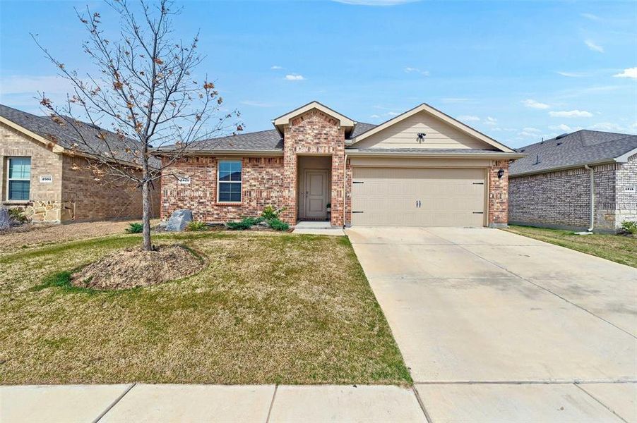 View of front of home with brick siding, a garage, concrete driveway, and a front lawn