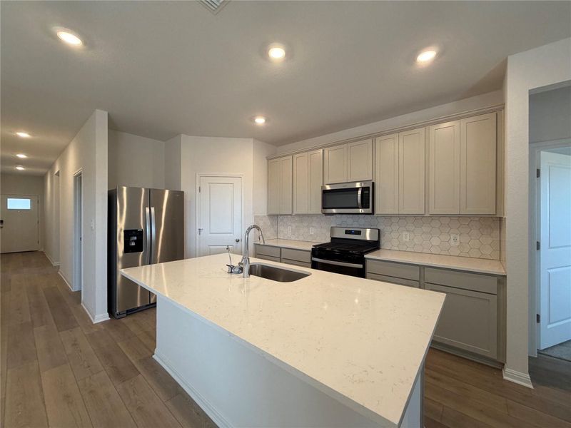 Kitchen with stainless steel appliances, light stone counters, a center island with sink, tasteful backsplash, and recessed lighting