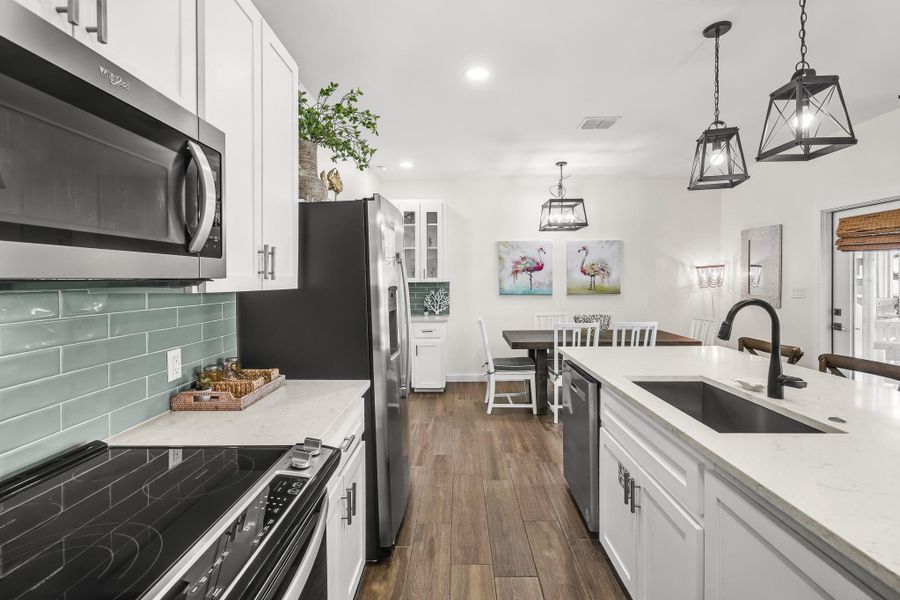 Kitchen with stainless steel appliances, white cabinetry, light stone counters, hanging light fixtures, and dark wood finished floors Kitchen with stainless steel appliances, white cabinetry, light stone counters, hanging light fixtures, and dark wood finished floors