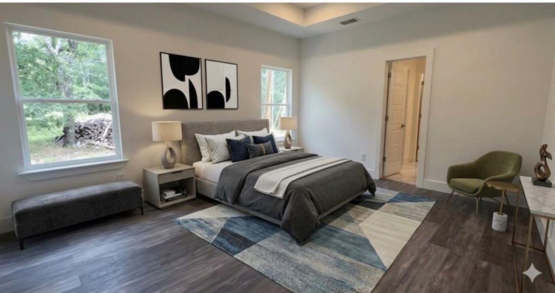 Spacious bedroom featuring wood-finish flooring, two large windows, a tray ceiling, and a doorway