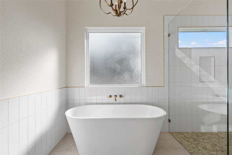 Bathroom featuring tile walls, a freestanding tub, a tile shower, wainscoting, and a textured wall Bathroom featuring tile walls, a freestanding tub, a tile shower, wainscoting, and a textured wall