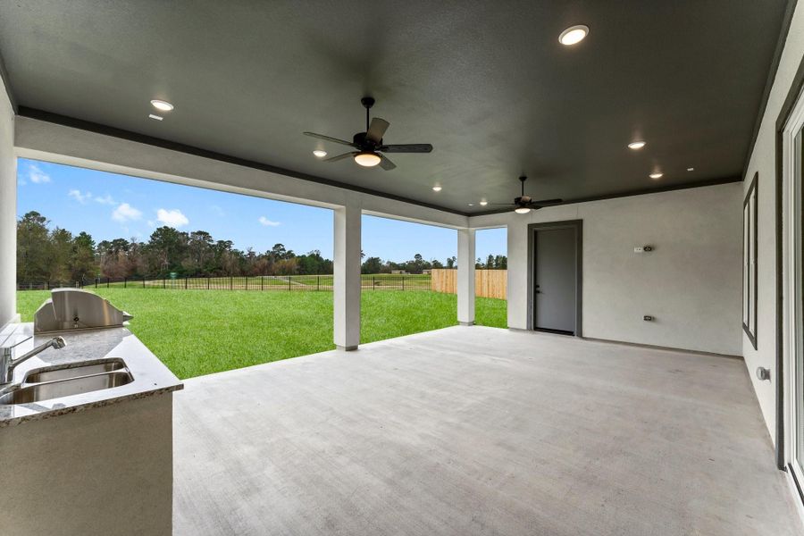 This photo showcases a spacious covered patio with ceiling fans and recessed lighting, overlooking a large, fenced backyard. An outdoor kitchen with a sink and countertop provides a perfect space for entertaining. This photo showcases a spacious covered patio with ceiling fans and recessed lighting, overlooking a large, fenced backyard. An outdoor kitchen with a sink and countertop provides a perfect space for entertaining.