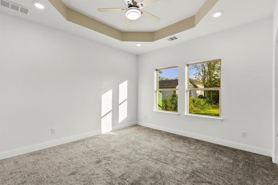 Carpeted spare room featuring ceiling fan and a raised ceiling