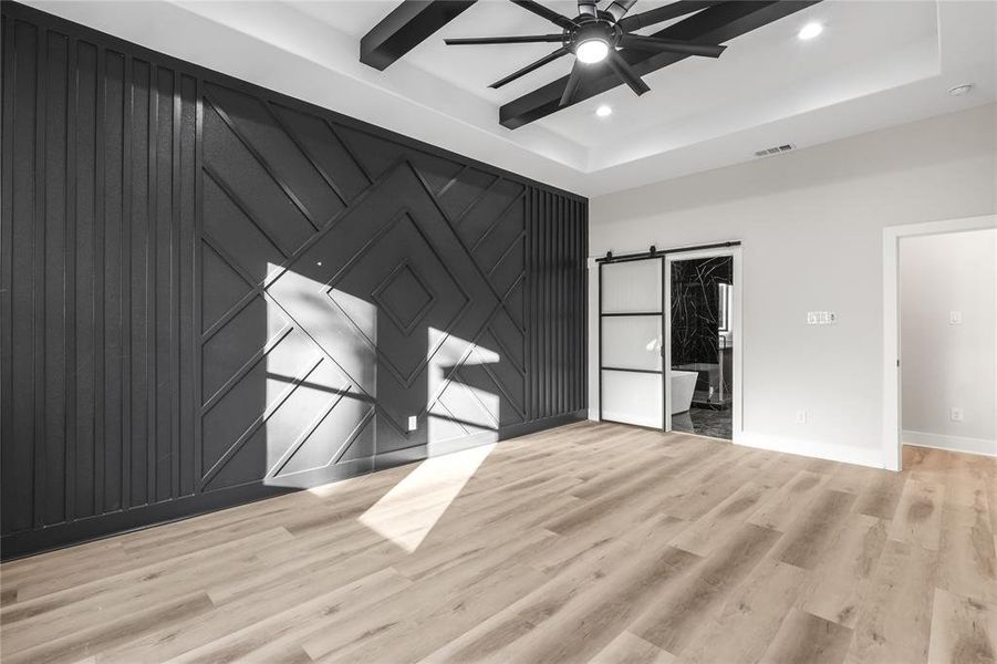 Unfurnished room featuring ceiling fan, a barn door, a tray ceiling, and light hardwood / wood-style flooring