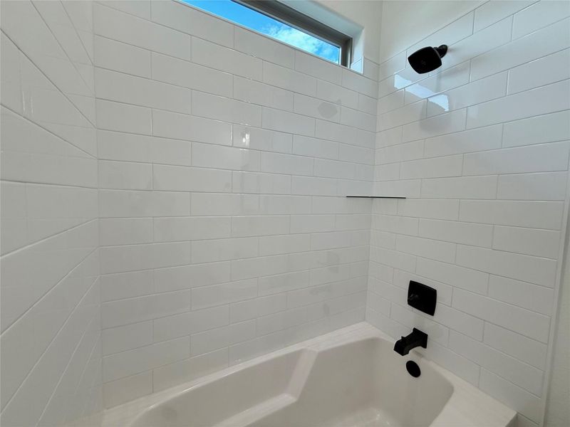 White subway tile surround with a built-in tub, matte black shower fixtures, and a transom window